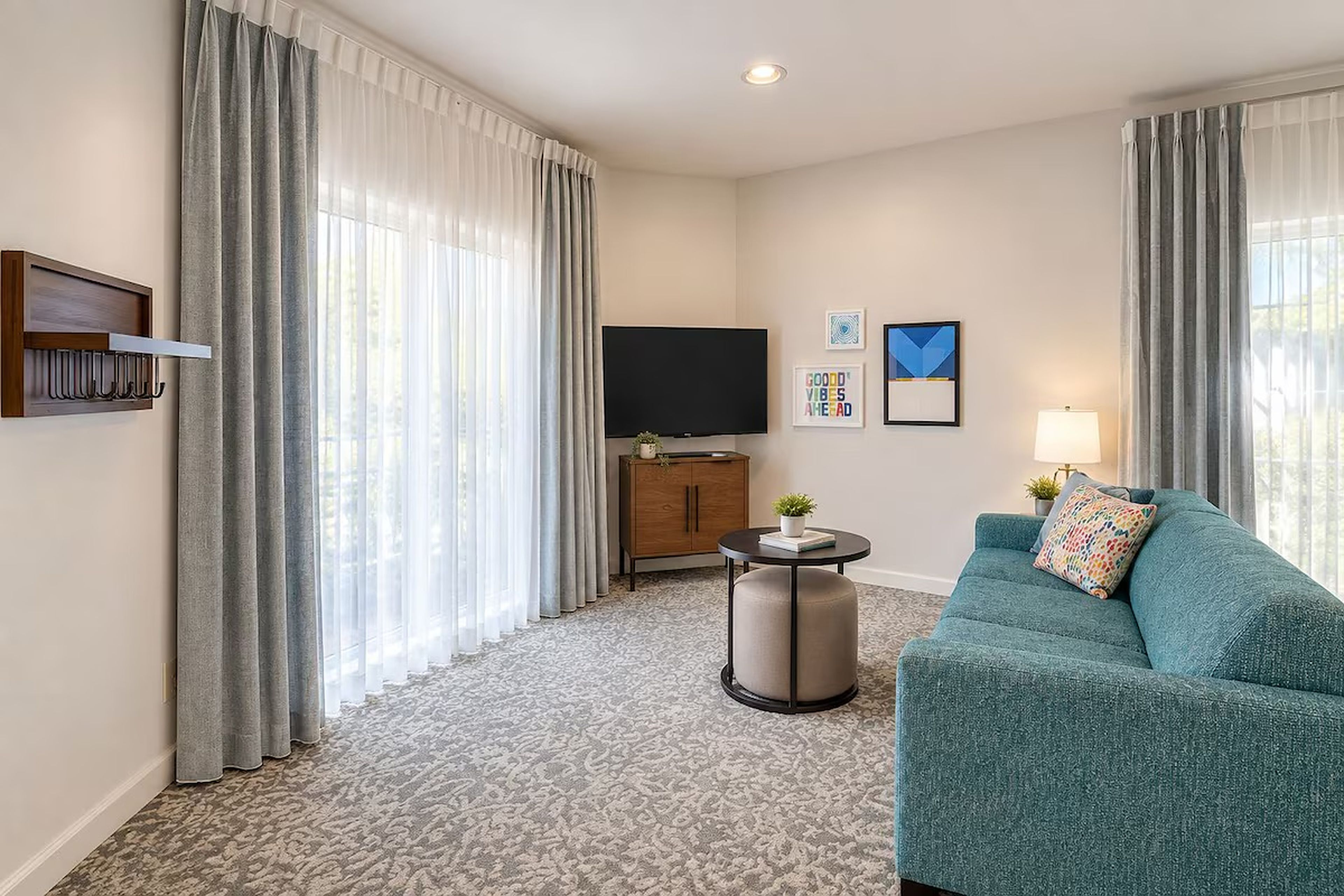 A hotel room with a sofa, a television, a small table with a plant, and a wall-mounted TV stand.