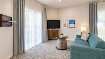A hotel room with a sofa, a television, a small table with a plant, and a wall-mounted TV stand.