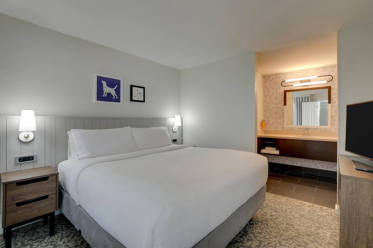 Habitación de hotel con una cama grande, lámparas de noche, un televisor, un espejo y obras de arte en la pared.