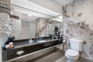 Un bany modern amb un rebedor de marbre, una superfície de taulell negra, un vàter blanc i un mirall gran.