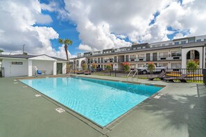 A rectangular swimming pool with clear blue water, surrounded by a concrete deck. There are lounge chairs and a small white building with a door and windows. - Quality Inn & Suites Orlando East - UCF Area (Orlando)