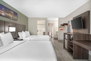 Une chambre d’hôtel avec deux lits, une télévision, un bureau et une salle de bain visible à travers une porte ouverte.