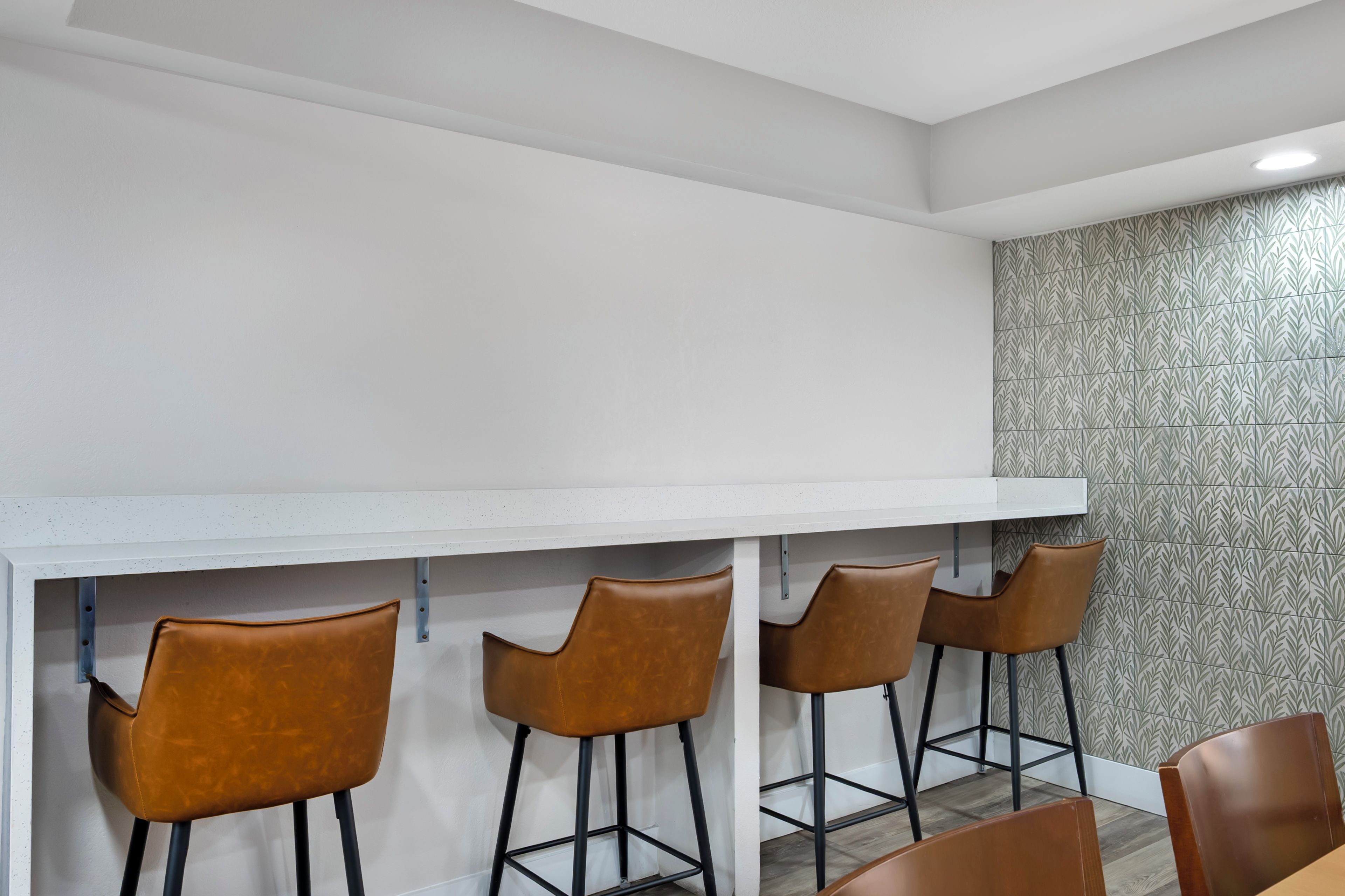 A bar area with a white countertop and four brown chairs.