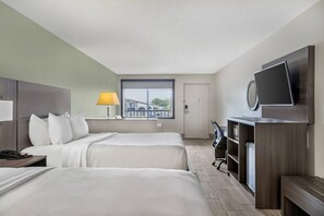 Une chambre d’hôtel avec deux lits, un bureau, une chaise, une télévision et une fenêtre donnant sur des immeubles.