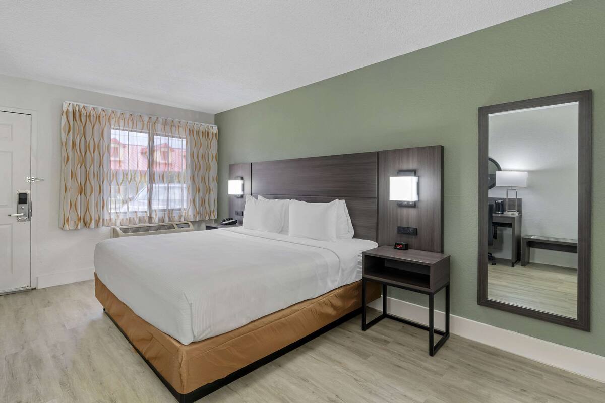 A hotel room with a large bed, bedside tables, a mirror, and a view of the outside.
