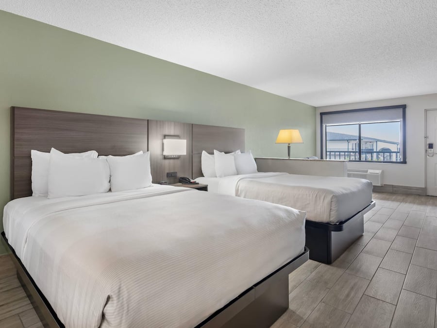 Quarto de hotel com duas camas, uma escrivaninha, uma cadeira e uma janela com vista.