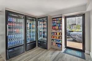A row of beverage vending machines with a variety of drinks, a snack shelf stocked with chips and snacks, and a view of a parked car outside. - Quality Inn & Suites Orlando East - UCF Area (Orlando)