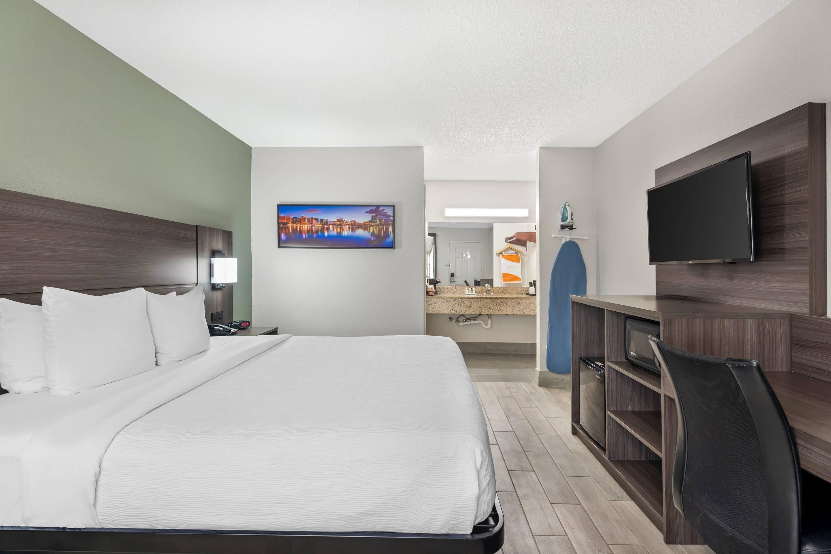 Habitación de hotel con una cama, un escritorio, un televisor y un baño a la vista.