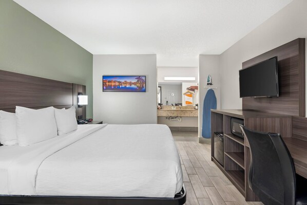 Une chambre d’hôtel avec un lit, un bureau, une télévision et une salle de bain que l’on aperçoit à l’arrière-plan.