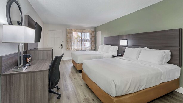 A hotel room with a desk, two beds, a TV, and a window with curtains.