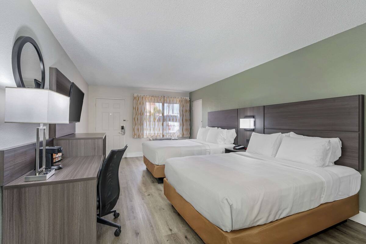 A hotel room with a desk, two beds, a TV, and a window with curtains.