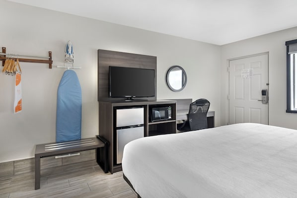A hotel room with a bed, a television, a microwave, a bench, and a door.