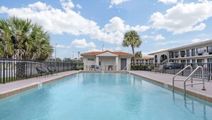 A swimming pool with a small building in the background, surrounded by palm trees and a fence.