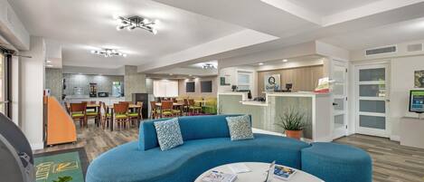 A modern interior with a curved blue sofa, a round coffee table with magazines, and a kitchen area in the background.