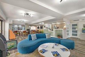 A modern interior with a curved blue sofa, a round coffee table with magazines, and a kitchen area in the background. - Quality Inn & Suites Orlando East - UCF Area (Orlando)