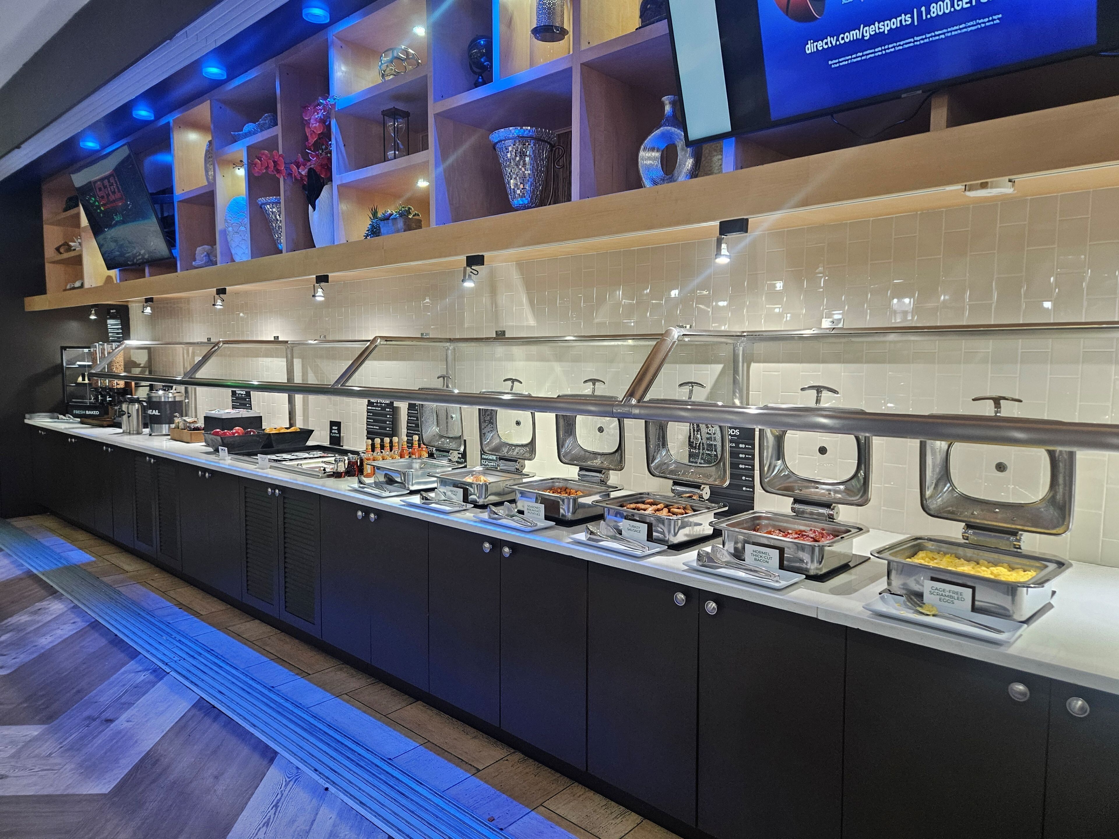 A buffet area with various food stations, a coffee machine, and a television displaying a sports channel.
