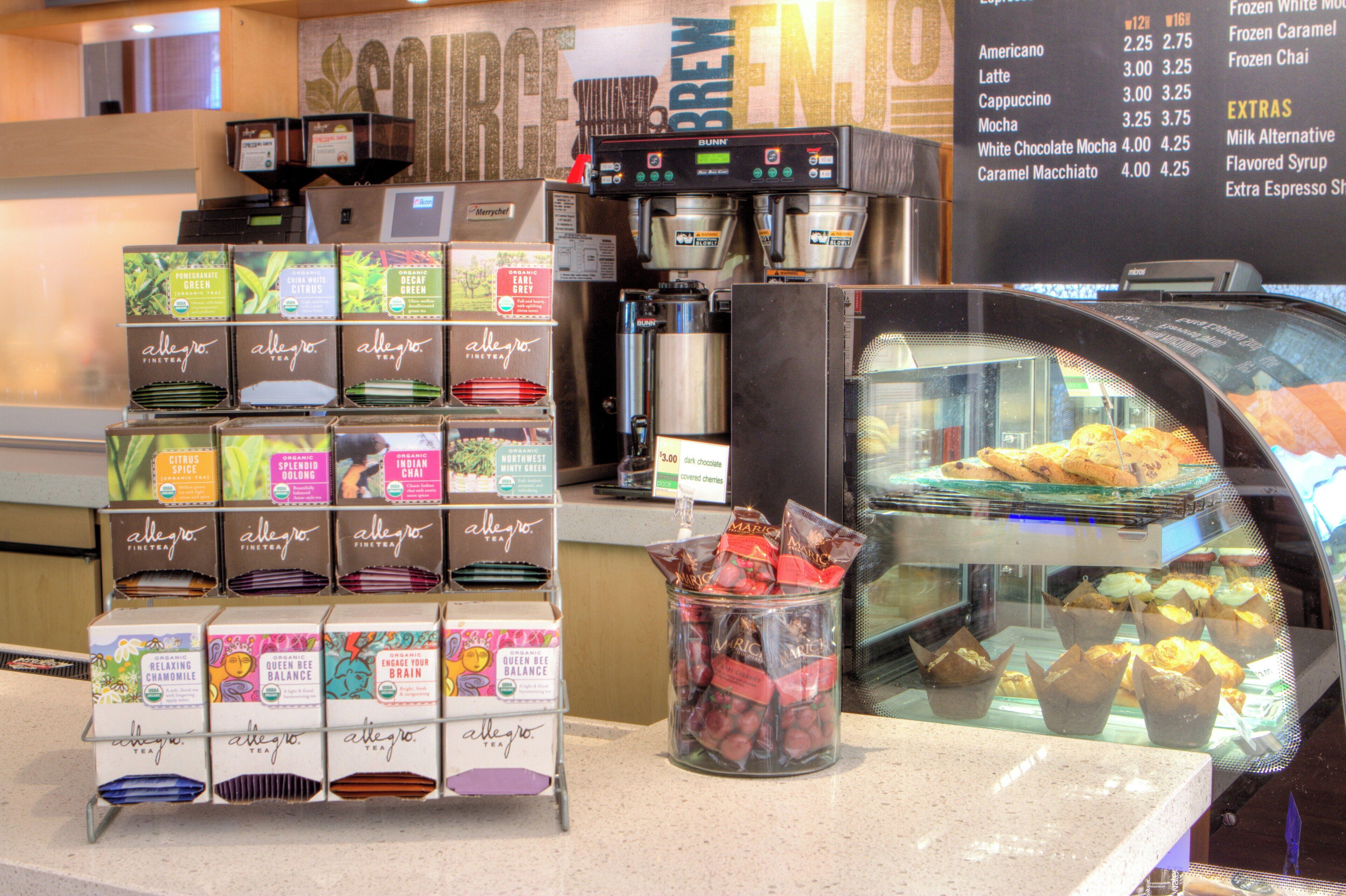 A coffee shop counter with a variety of tea boxes, a coffee machine, and a display case with pastries.