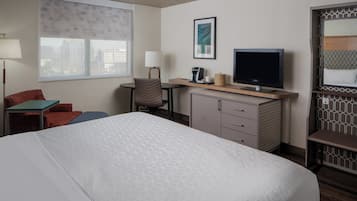 A hotel room with a bed, a desk with a television, a chair, a lamp, and a window with a city view.