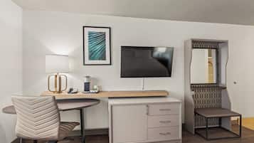 Una habitación de hotel con escritorio, silla, televisión, armario y cama.