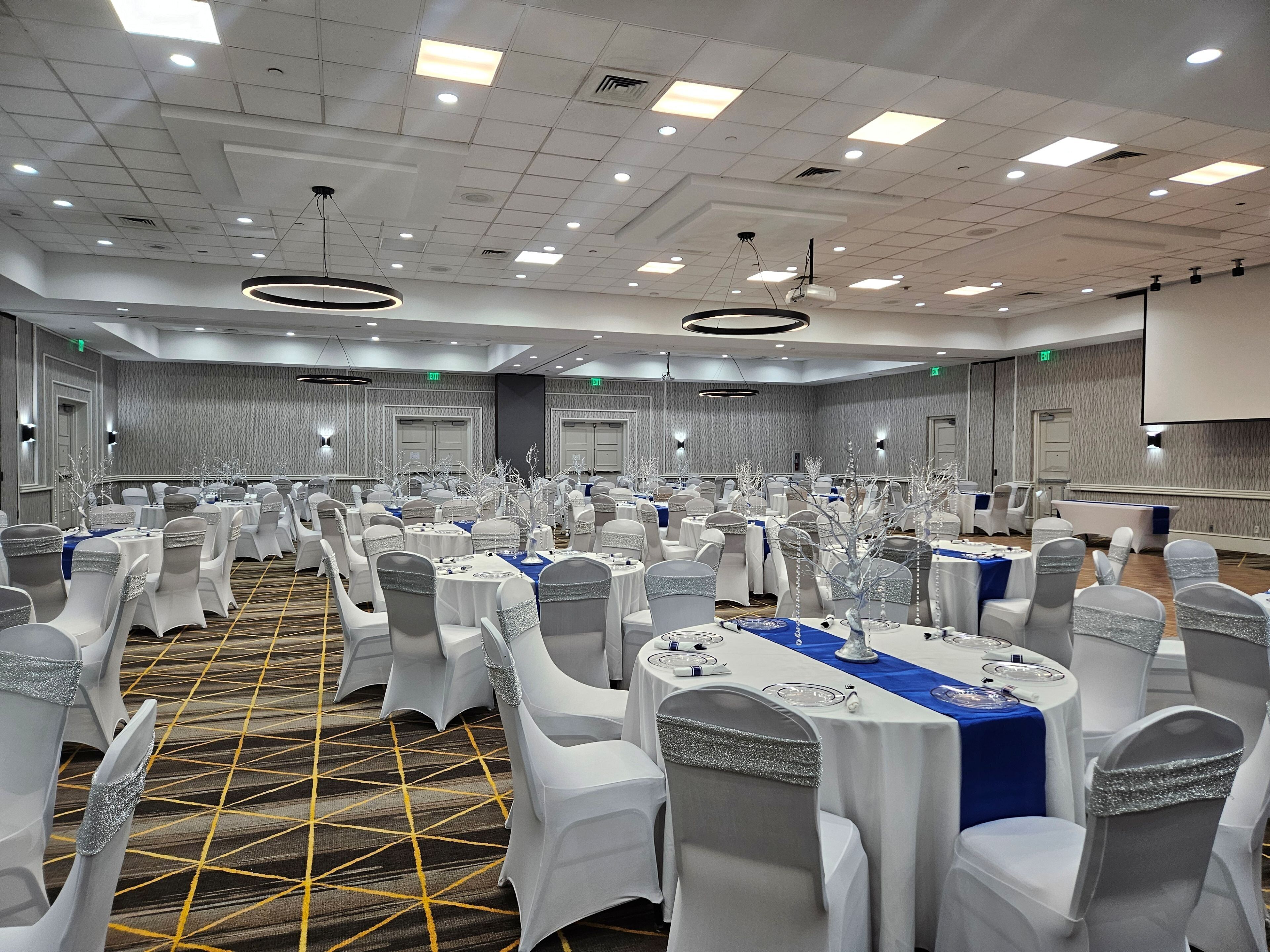 A banquet hall with round tables, white chairs, and a carpeted floor.
