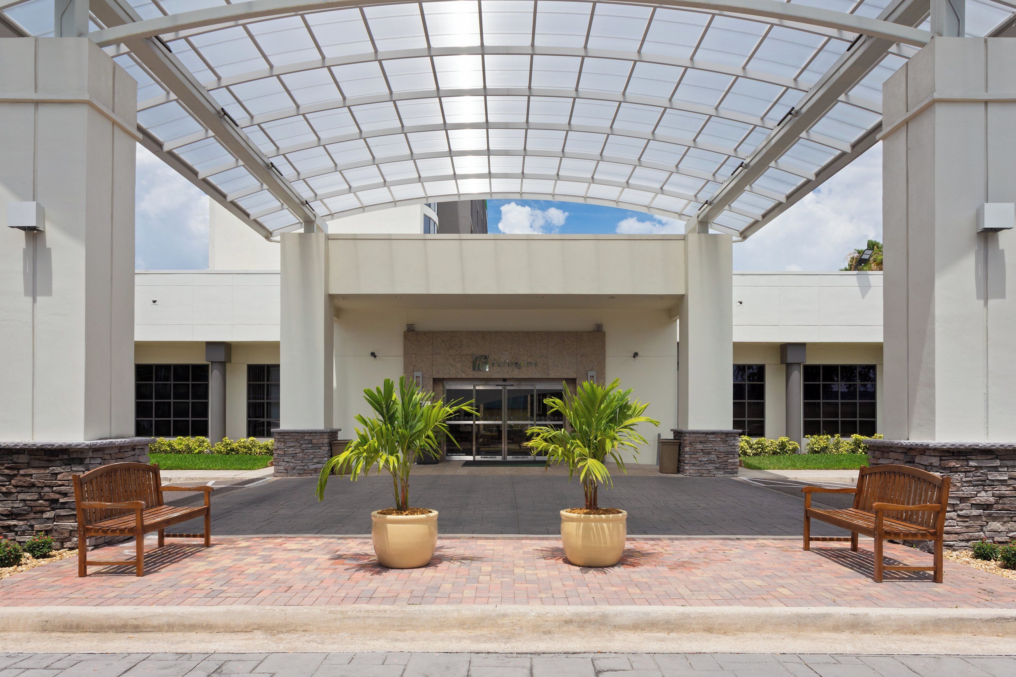 A covered entrance with a glass roof, two potted plants, and wooden benches.