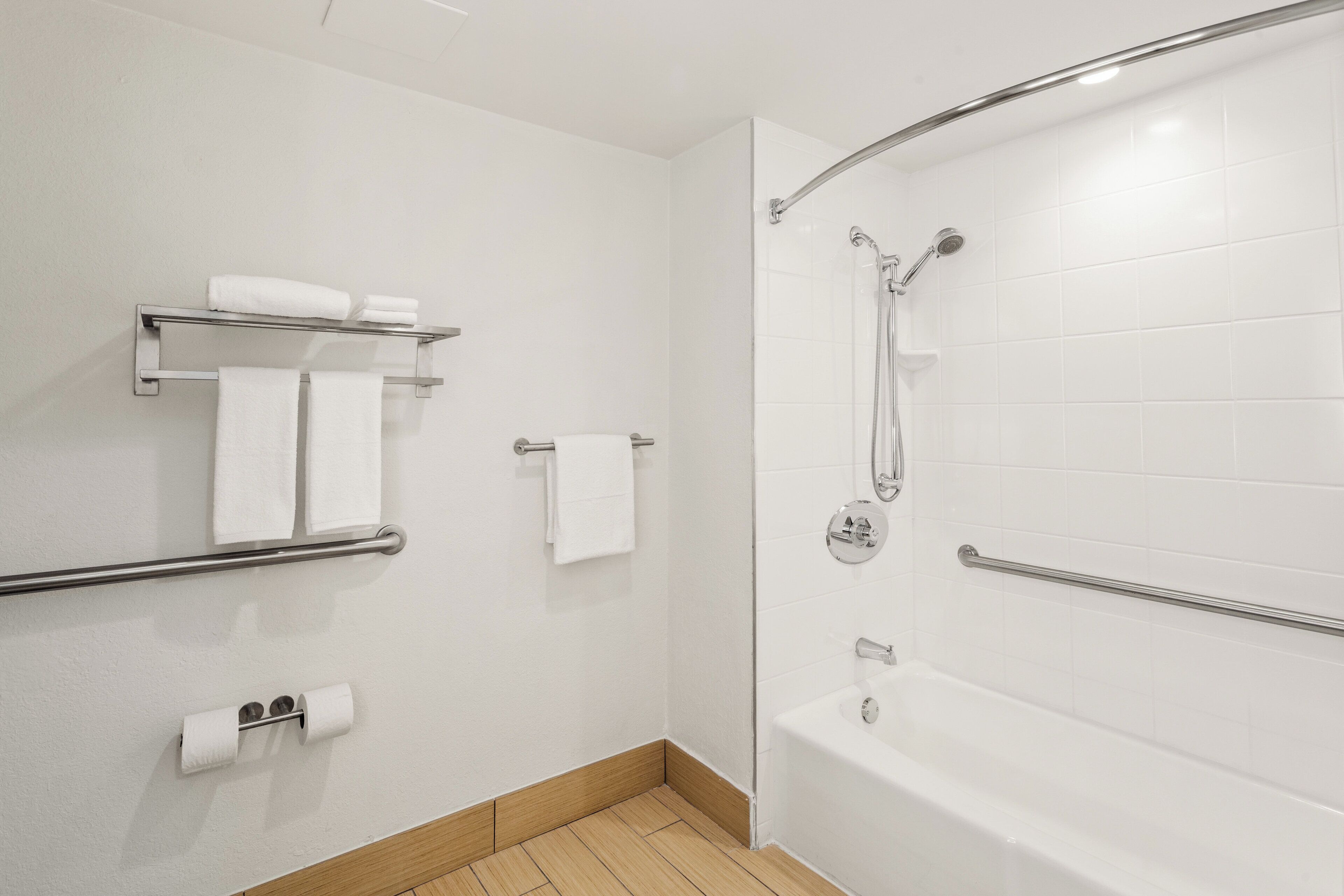 A modern bathroom with a bathtub, shower, and toilet paper holder.