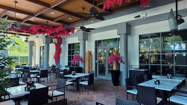 An outdoor dining area with tables and chairs, a bar entrance, and decorative plants. - Holiday Inn Tampa Westshore - Airport Area by IHG (Tampa)