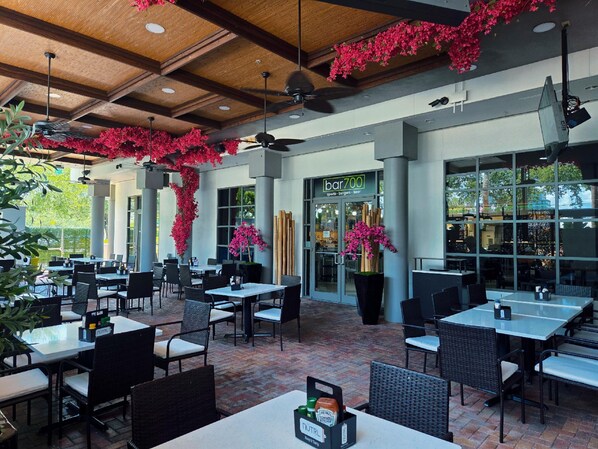 An outdoor dining area with tables and chairs, a bar entrance, and decorative plants. - Holiday Inn Tampa Westshore - Airport Area by IHG (Tampa)