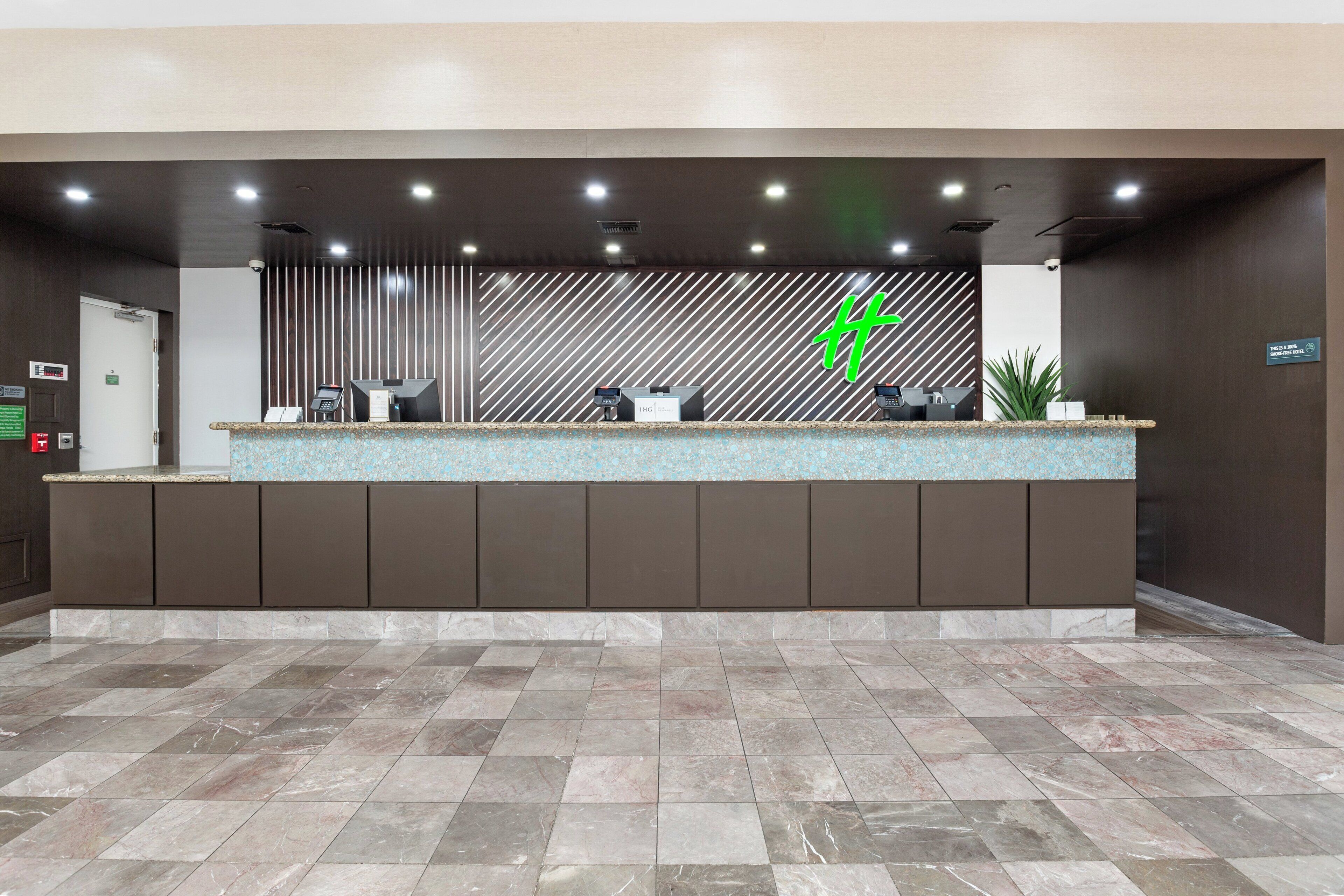 Un mostrador de recepción con un fondo estampado, una pantalla digital y una planta en maceta.