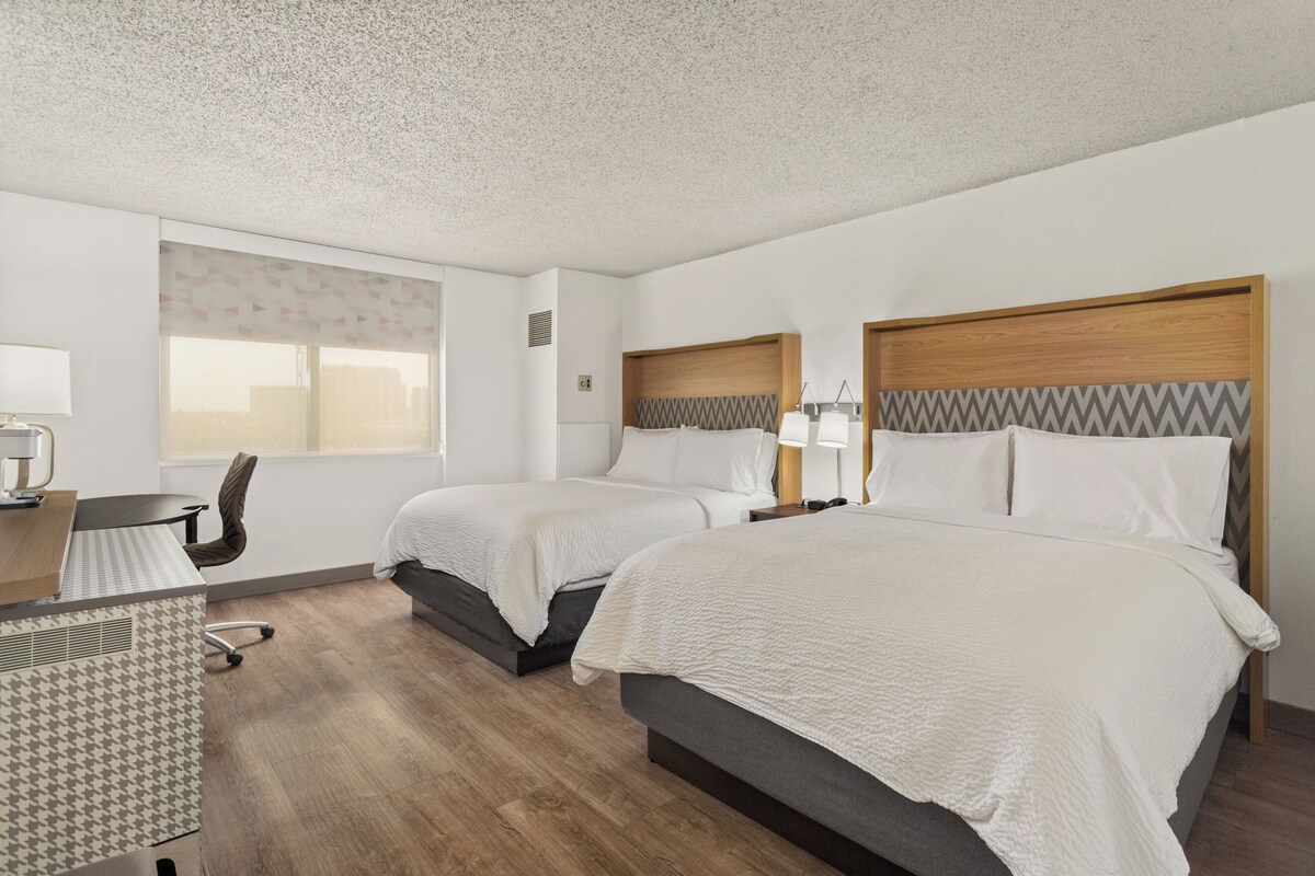 Habitación de hotel con dos camas, un escritorio, una silla y una ventana.