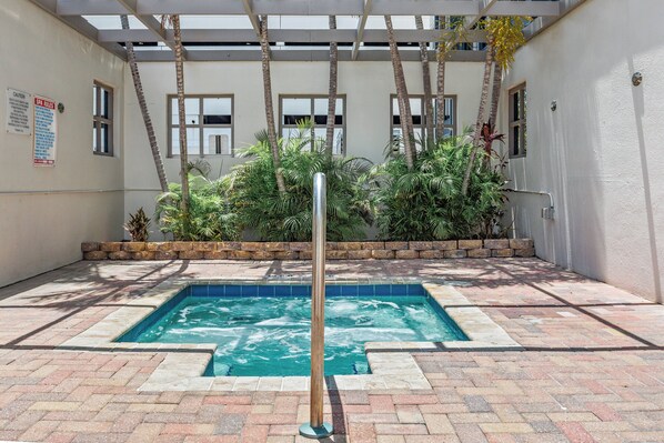 Una piscina con un poste metálico en el centro, rodeada por un patio de ladrillo y palmeras.