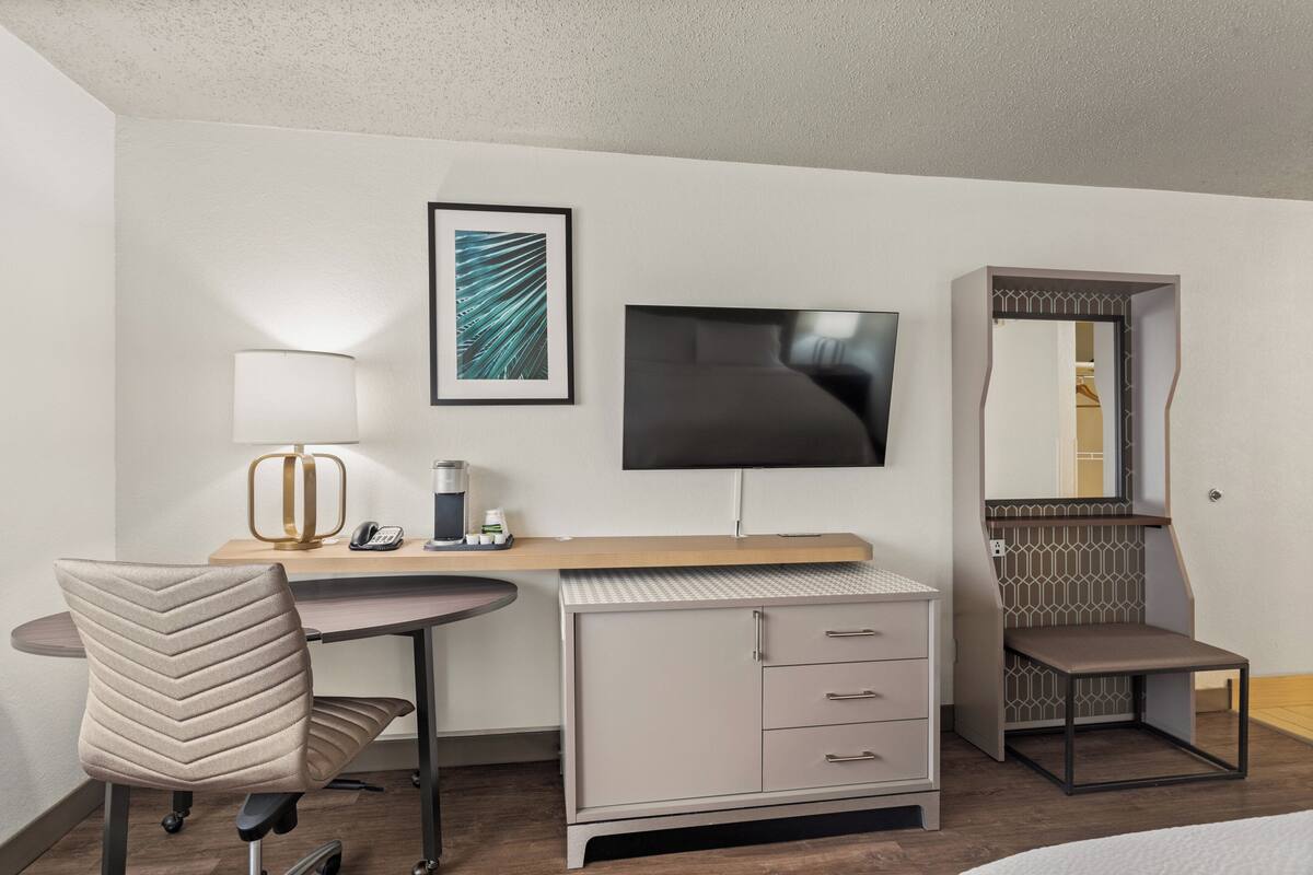 A hotel room with a desk, chair, TV, wardrobe, and a bed.