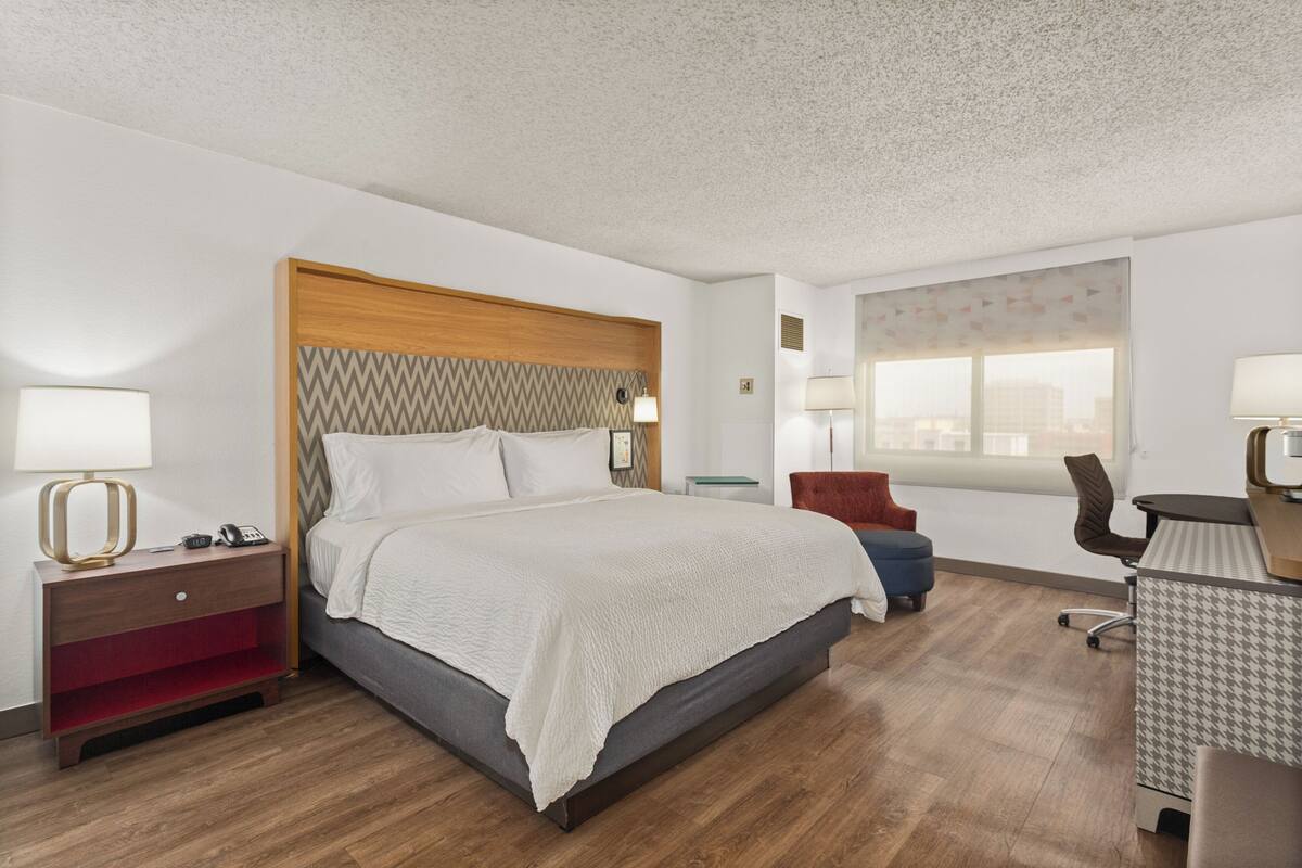 A hotel room with a bed, a desk, a chair, and a window.