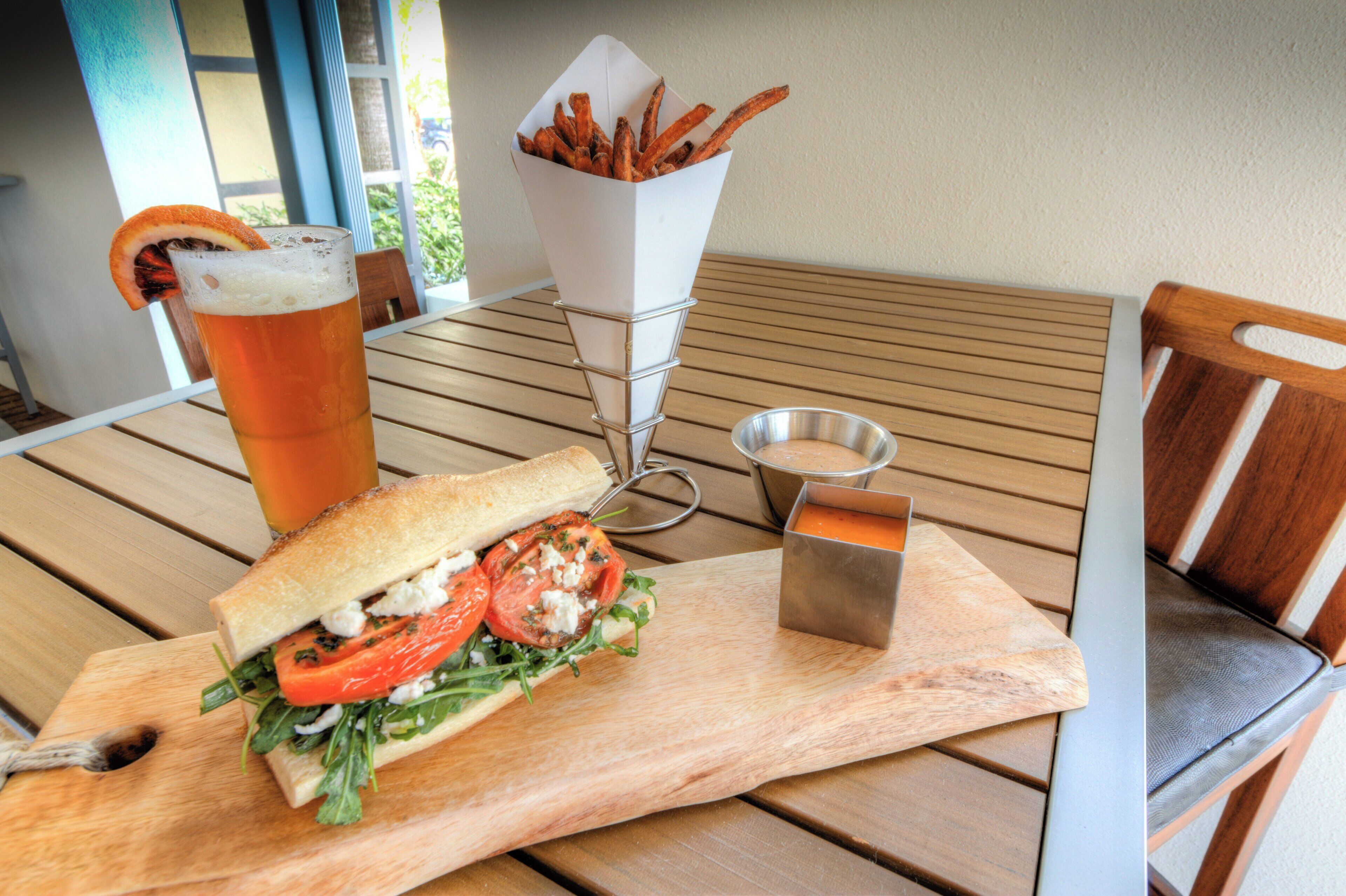 Un repas composé d’un sandwich, de frites, d’une boisson et d’un petit récipient de sauce, le tout servi sur une table en bois.