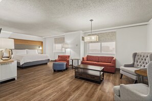 Una habitación de hotel con una cama, un sofá, una silla, una mesita de café y una lámpara.