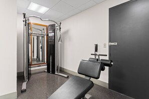 Un gimnasio con una banca, máquina de pesas y una puerta.