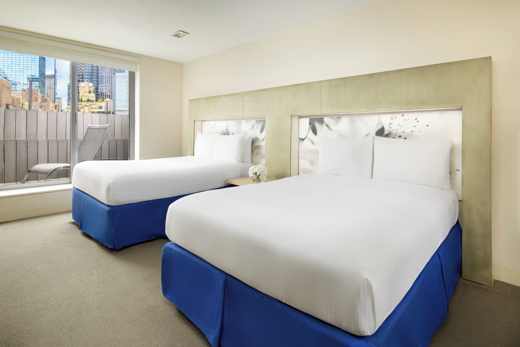 A hotel room with two beds, a large window with a city view, and a wooden partition.