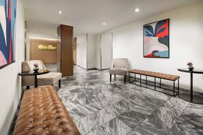 A modern lobby with a marble floor, a brown tufted bench, a wooden panel wall, and a colorful abstract painting. - The Shoreham (New York)
