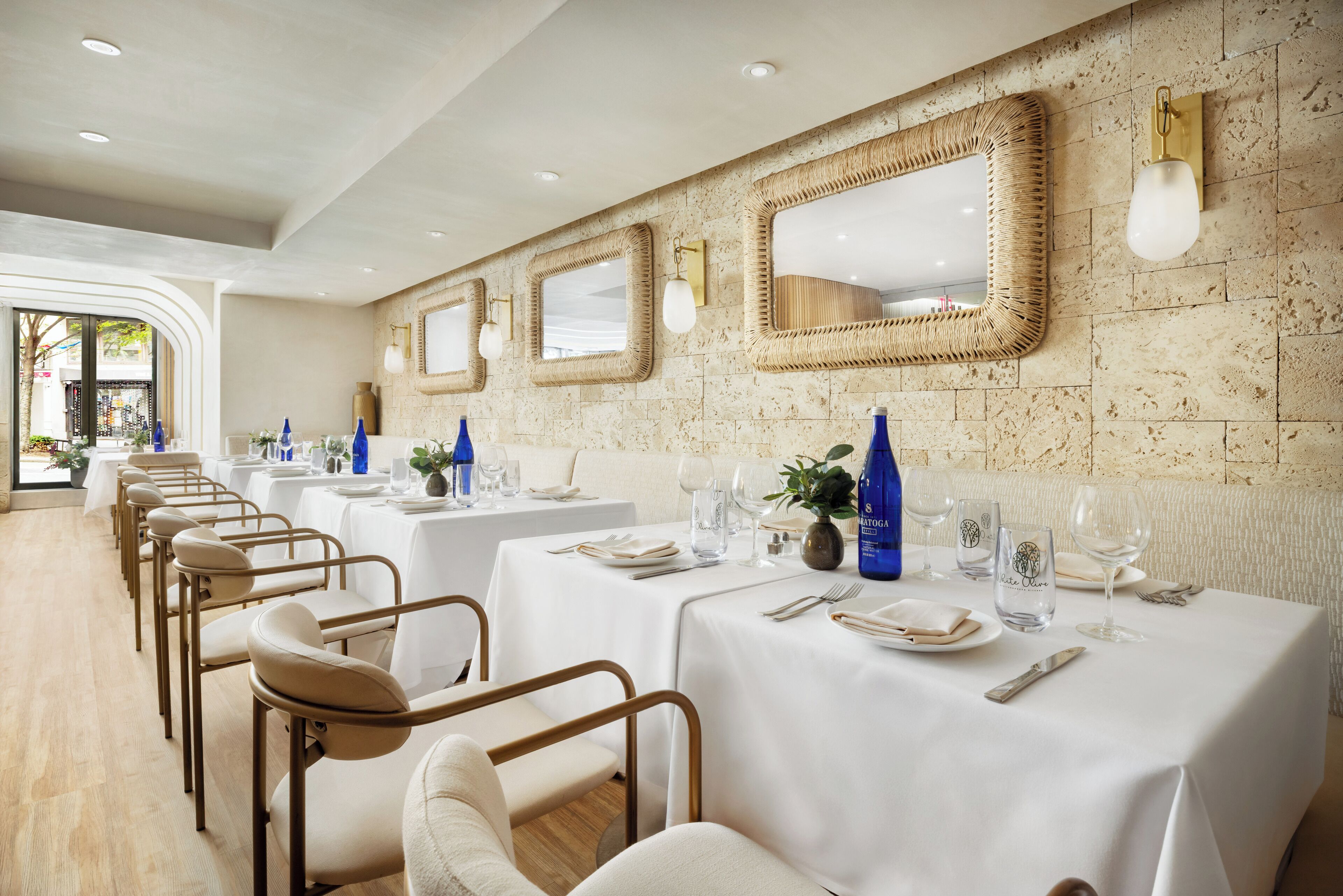 A dining area with white tablecloths, gold-framed mirrors, and blue bottles on the tables.