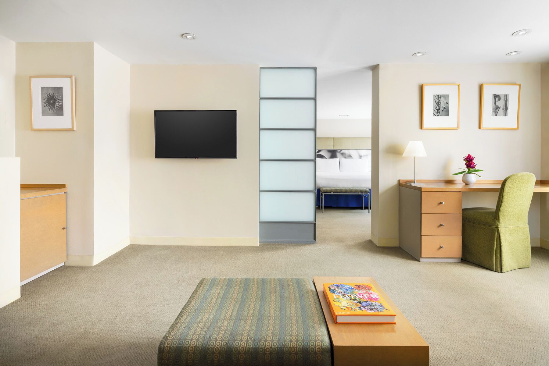 Une chambre d’hôtel équipée d’une télévision à écran plat, d’un bureau avec une chaise, d’un lit et d’une petite table sur laquelle se trouve un livre.