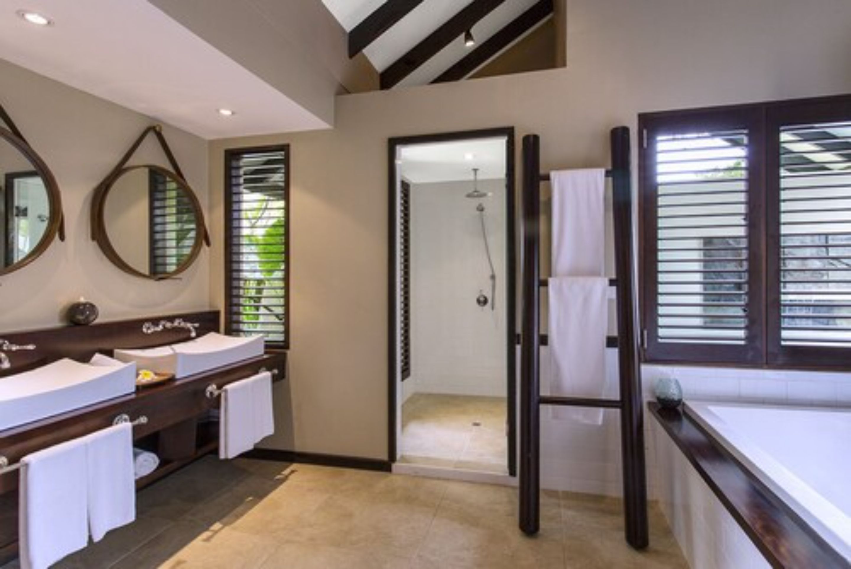 A modern bathroom with a double sink vanity, a glass shower enclosure, and a large window with blinds.