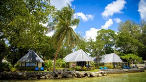 A resort with multiple bungalow-style buildings, a palm tree, and a clear blue sky. - Warwick Le Lagon - Vanuatu (Port Vila)