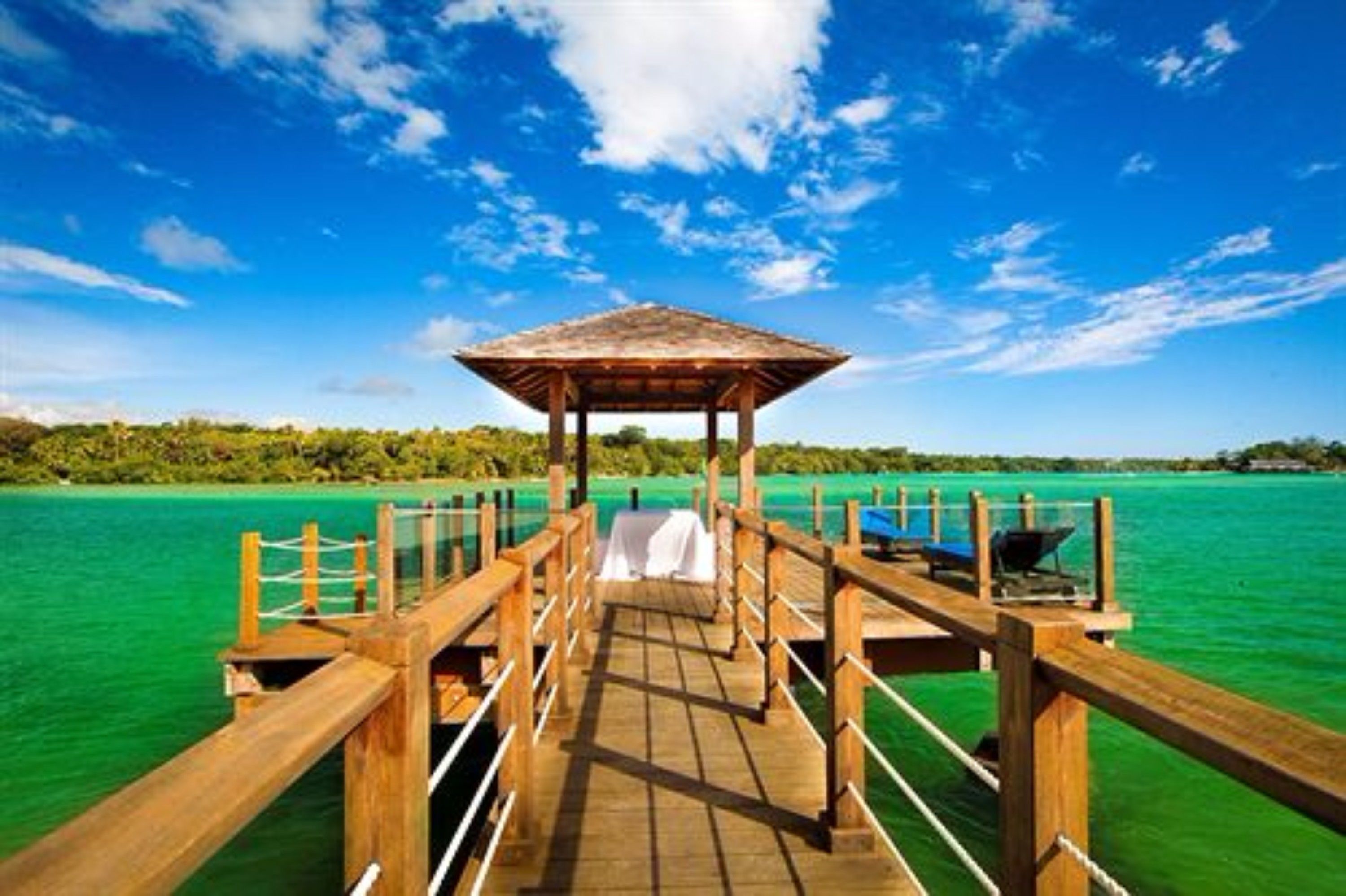 A wooden pier leading to a gazebo over turquoise water, surrounded by lush greenery.