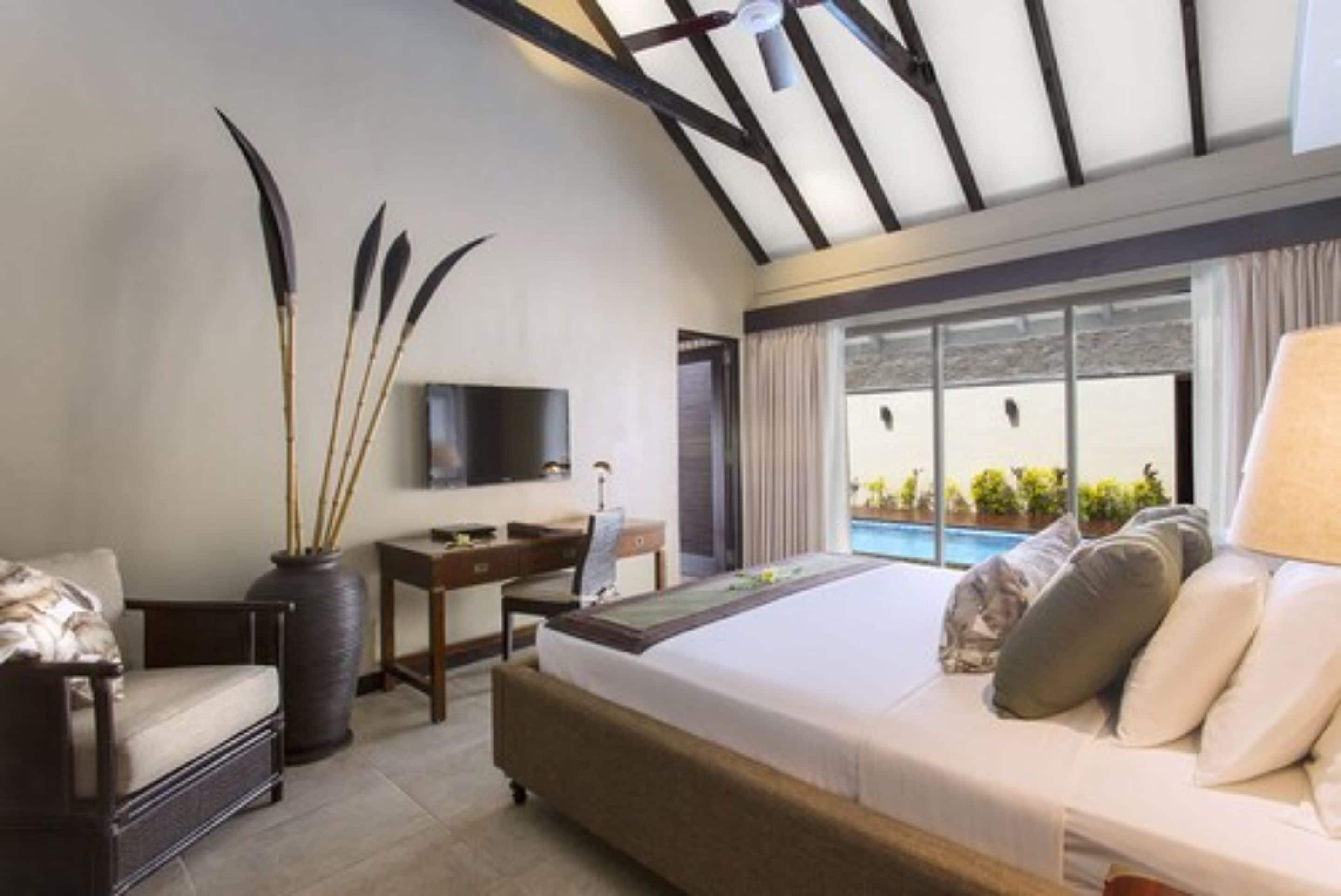 A hotel room with a bed, a desk, a chair, a TV, and a view of a swimming pool.