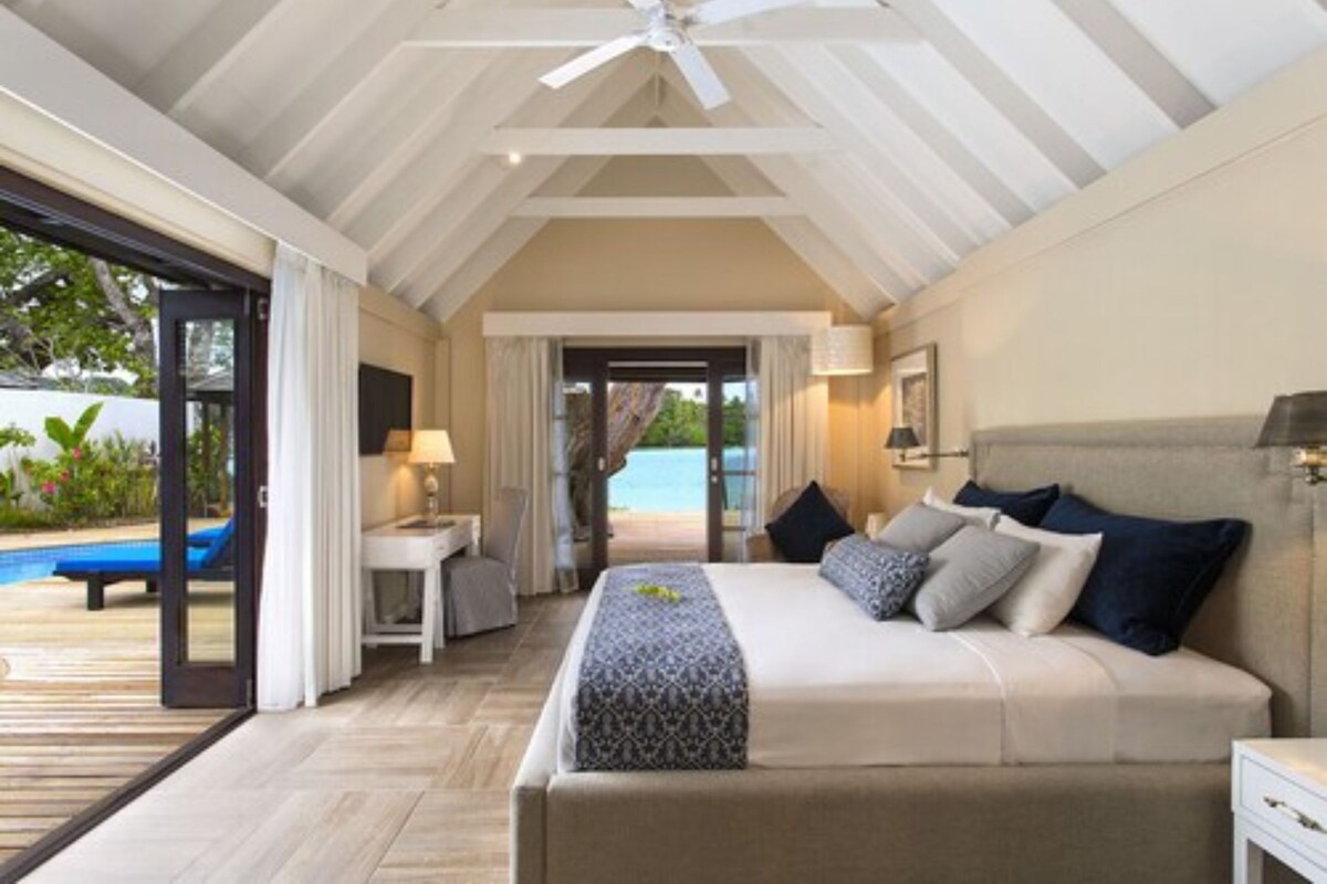 A bedroom with a bed, bedside table, lamp, and a view of a pool and outdoor area.