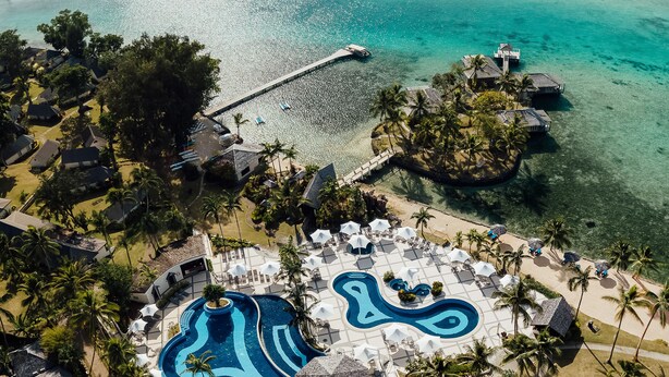 An aerial view of a resort with a large swimming pool, beach umbrellas, and palm trees. - Warwick Le Lagon - Vanuatu (Port Vila)