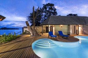 Ein Poolbereich mit Holzterrasse, Liegestuhl und einem kleinen Gebäude mit einem Strohdach.