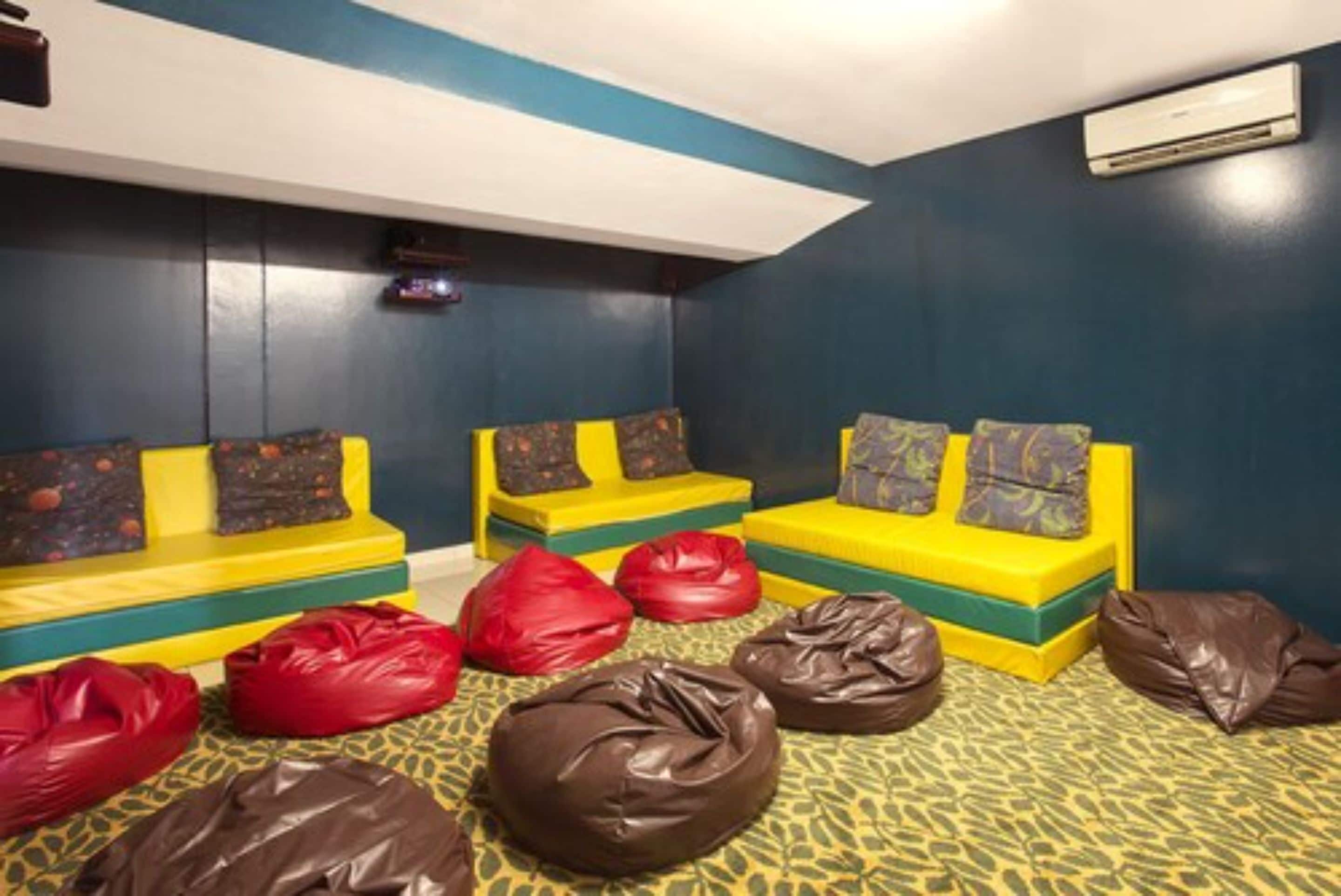 A room with yellow and green sofas, red and brown bean bags, and patterned carpet.