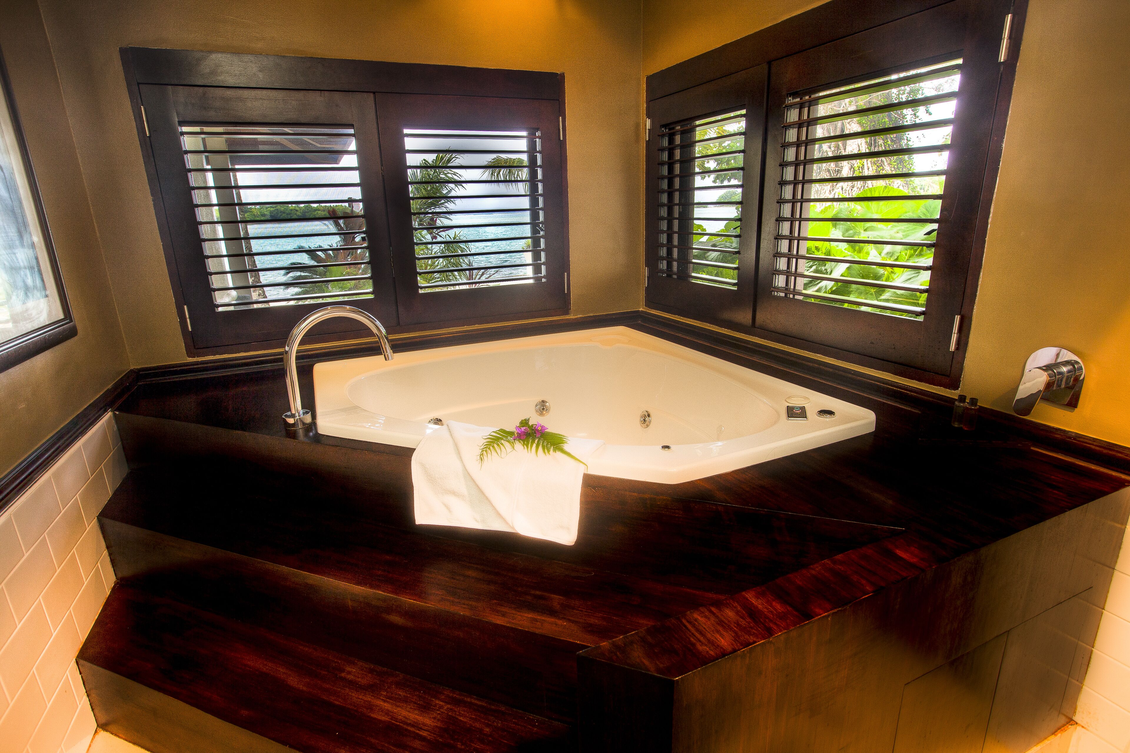 A modern bathroom with a freestanding bathtub, dark wood vanity, and large windows with blinds.