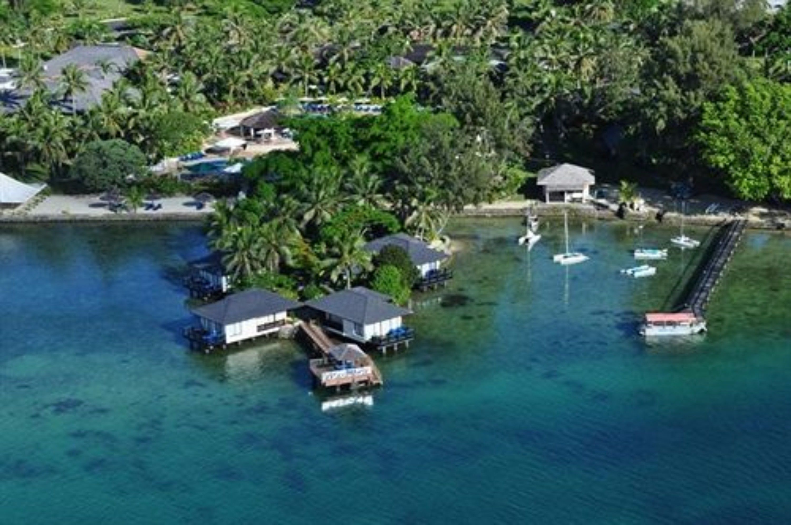 An aerial view of a tropical island with overwater bungalows, clear blue water, and a dock with boats.